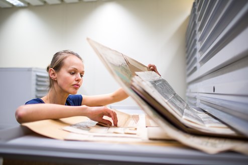 En kvinna studerar kartor i ett arkiv
